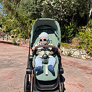 Irakli participe au concours pour gagner de l'argent avec cette photo : baby, stroller, sunglasses, hat, pacifier, outdoor, sunny, greenery, tree, road, baby_clothing, footwear, child, person, nature, shade, daylight, cute, modern, park