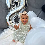 Jïa a rejoint le concours — aidez-le/la à gagner de superbes lots ! baby, child, smiling, dress, headband, balloon, number_balloon, silver_balloon, white_balloon, blanket, celebration, birthday, happy, sitting, cute, portrait, outdoor, person, festive, infant