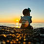 Merrin is registered to the contest to win money with this photo: baby, bow, sunset, beach, pebbles, ocean, water, sky, sun, silhouette, child, nature, outdoor, sitting, horizon, light, reflection, scenic, serene, calm