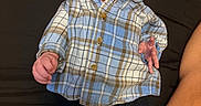 Benito is registered to the contest to win money with this photo: baby, infant, plaid_shirt, blue_shirt, black_pants, white_socks, lying_down, curious_expression, indoor, person, child, human, skin, face, hand, legs, casual_clothing, portrait, newborn, relaxed