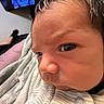 Benito is registered to the contest to win money with this photo: baby, close_up, face, blanket, indoor, person, portrait, curious, expression, clothing, television, blurred_background, head, skin, human, infant, sleepwear, texture, young_child, indoors