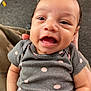 baby, child, smiling, face, onesie, polka_dot, grey_clothing, hand, carpet, toy, indoor, person, camouflage_pants, happy, cute, infant, portrait, closeup, skin, expression