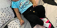 Rosalia is registered to the contest to win money with this photo: baby, bedspread, black_pants, blue_shirt, bright_colors, child, cozy, curly_hair, cute, happy, indoors, infant, lying_down, patterned_bed, person, pillow, portrait, smiling, socks, unicorn