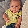 baby, child, polo_shirt, yellow_clothing, plush_toy, panda_toy, couch, soft_furniture, curious_eyes, infant, hand, face, portrait, indoors, comfortable, cute, young_child, fabric, striped_cloth, relaxed
