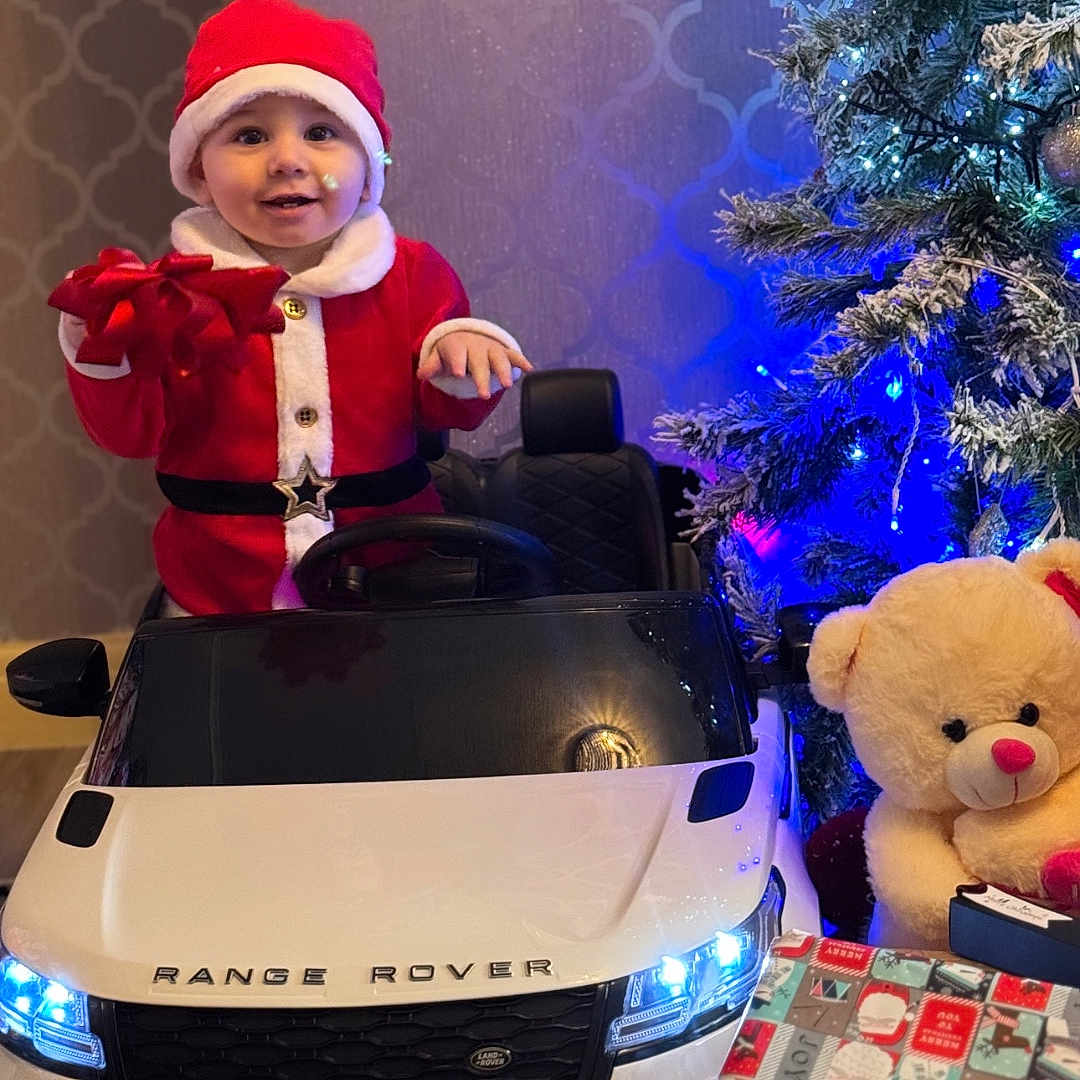 Leandros joined the competition — help win amazing prizes! celebration, child, christmas_lights, christmas_tree, decor, festive, gift_wrapping, happy, holiday, indoor, present, range_rover, red_clothing, santa_claus_costume, smiling, teddy_bear, toddler, toy, toy_car, white_fur_trim