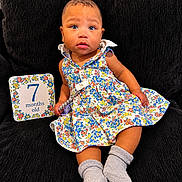 Navi joined the competition — help win amazing prizes! baby, child, 7_months_old, blue_eyes, floral_dress, socks, couch, milestone_card, indoor, portrait, cute, infant, sitting, clothing, person, face, head, expression, comfort, colorful