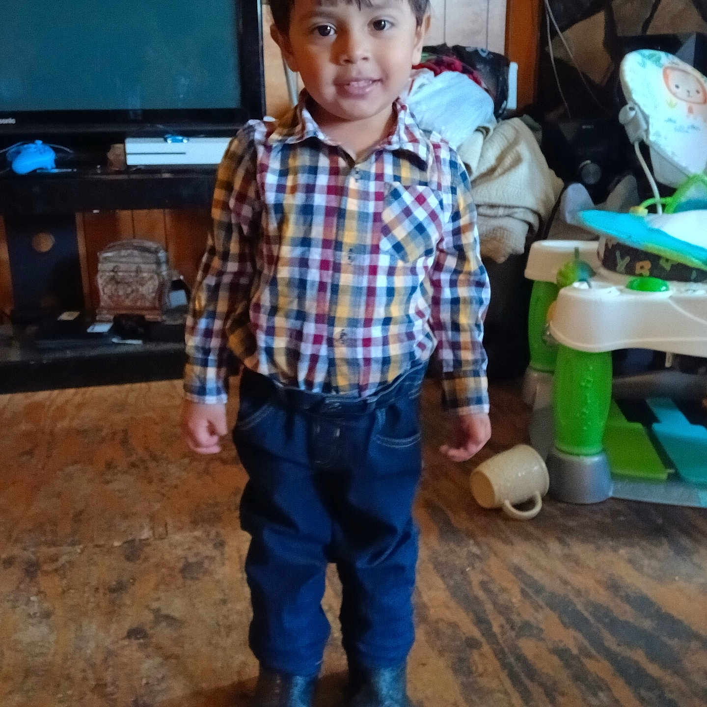 Israel joined the competition — help win amazing prizes! child, boy, plaid_shirt, blue_jeans, boots, indoor, floor, wood_paneling, television, furniture, baby_toy, smile, standing, young, casual_clothing, home, cozy, cluttered, person, portrait
