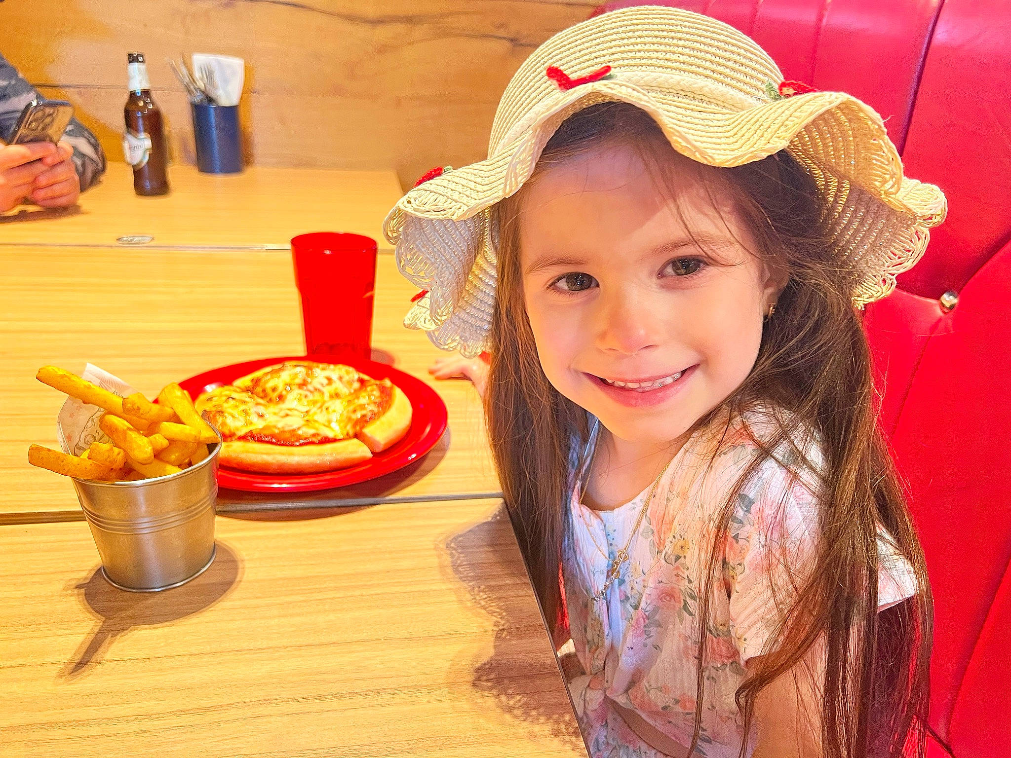 Daria is registered to the contest to win money with this photo: automotive_tire, child, cuisine, dish, fast_food, food, happy, hat, headgear, ingredient, joy, motor_vehicle, person, plate, recipe, red, smile, sweetness, table, tableware