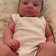 Arabella is registered to the contest to win money with this photo: baby, infant, white_onesie, cushion, floral_pattern, indoor, person, skin, legs, arms, face, expression, sitting, natural_light, closeup, newborn, child, young, cute, comfort