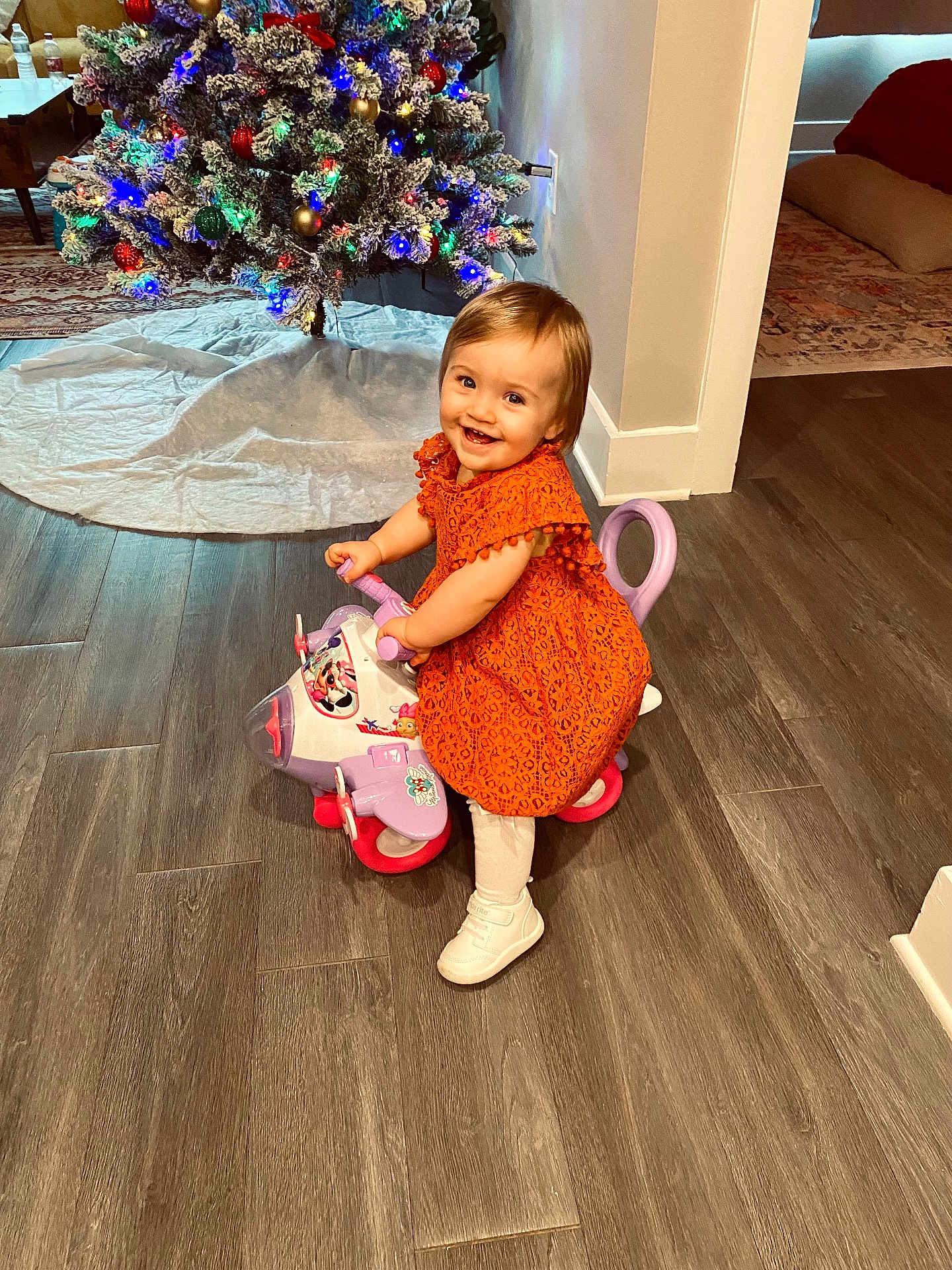 Sawyer joined the competition — help win amazing prizes! toddler, child, orange_dress, toy_airplane, smile, indoor, christmas_tree, holiday, decorations, wooden_floor, happy, person, play, festive, home, flooring, lighting, cute, small_child, holiday_lights