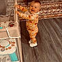Sawyer is registered to the contest to win money with this photo: toddler, child, pajamas, smiling, playpen, floor, rug, living_room, sofa, wooden_table, toy, happy, indoor, baby, footwear, patterned_clothing, wood_floor, furniture, home, cute