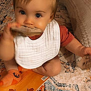 Sawyer joined the competition — help win amazing prizes! baby, child, bib, orange_socks, wooden_block, carpet, rug, pillow, indoor, playing, cute, toddler, sitting, curious, hand, footwear, patterned_rug, soft_lighting, home, exploration