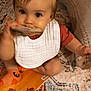 baby, child, bib, orange_socks, wooden_block, carpet, rug, pillow, indoor, playing, cute, toddler, sitting, curious, hand, footwear, patterned_rug, soft_lighting, home, exploration