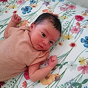 Lyana a rejoint le concours — aidez-le/la à gagner de superbes lots ! baby, newborn, infant, lying_down, striped_clothing, floral_pattern, bed_sheet, curious, fists, face, head, skin, person, indoors, cute, small, resting, soft_light, sleepwear, child
