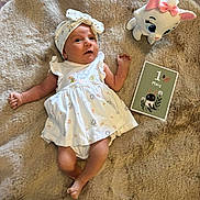 Elza participe au concours pour gagner de l'argent avec cette photo : baby, infant, dress, headband, plush_toy, cat_toy, milestone_card, fur_rug, soft_texture, lying_down, one_month, cute, child, indoors, celebration, portrait, white_clothing, small_hands, small_feet, curious_expression