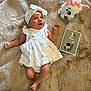 baby, infant, dress, headband, plush_toy, cat_toy, milestone_card, fur_rug, soft_texture, lying_down, one_month, cute, child, indoors, celebration, portrait, white_clothing, small_hands, small_feet, curious_expression