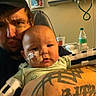 Jaylen joined the competition — help win amazing prizes! baby, adult, hospital_room, tattoo, medical_tape, medical_equipment, water_bottle, arm, person, infant, holding, face, expression, seated, indoor, clothing, headwear, healthcare, care, closeup