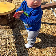 Jaylen is registered to the contest to win money with this photo: toddler, child, blue_sweatshirt, clapping, playground, wood_chips, outdoor, daylight, shadow, equipment, person, curious, pants, sock, standing, young_child, casual_clothing, sunlight, expression, play