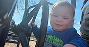 Jaylen is registered to the contest to win money with this photo: toddler, child, playground, steering_wheel, blue_sky, sunlight, outdoor, smiling, person, hand, clothing, tree, metal, daytime, happy, casual, fun, young_child, park, adult