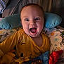 baby, child, smiling, happy, yellow_clothing, toy, pillow, blanket, indoor, face, portrait, infant, colorful, cute, expression, young_child, playtime, cozy, cushion, fabric