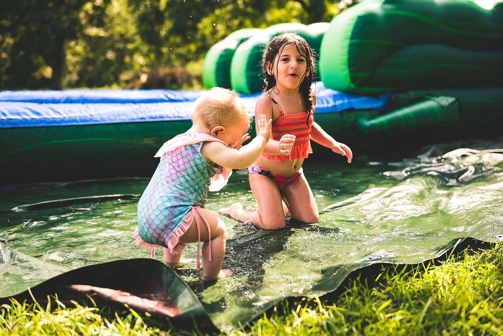 Addyson is registered to the contest to win money with this photo: child, event, fun, grass, happy, headwear, inflatable, leisure, outdoor_recreation, people_in_nature, person, personal_protective_equipment, plant, play, recreation, shorts, sitting, t_shirt, toddler, vacation