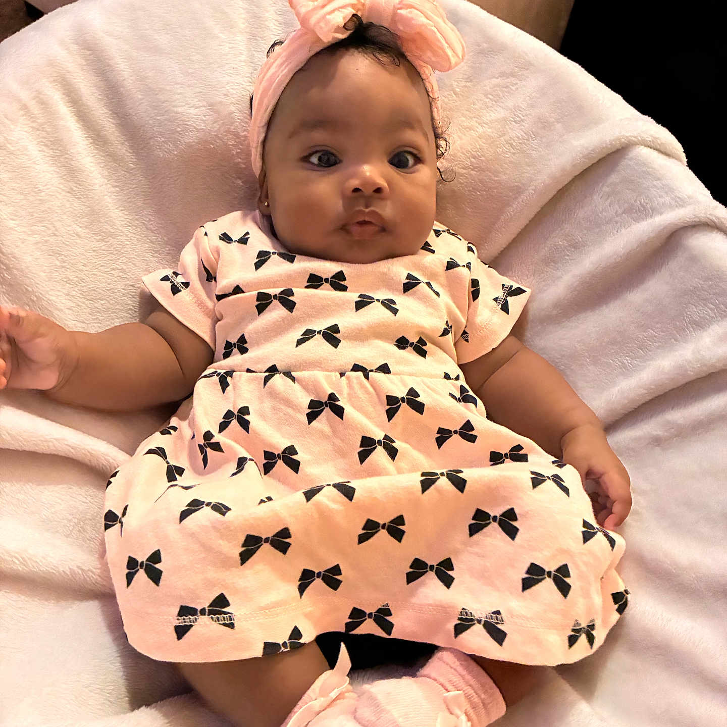 E Liah is registered to the contest to win money with this photo: baby, infant, child, pink_dress, headband, bow, socks, blanket, cozy, cute, portrait, indoors, soft_texture, clothing, smiling, person, baby_girl, comfortable, resting, adorable