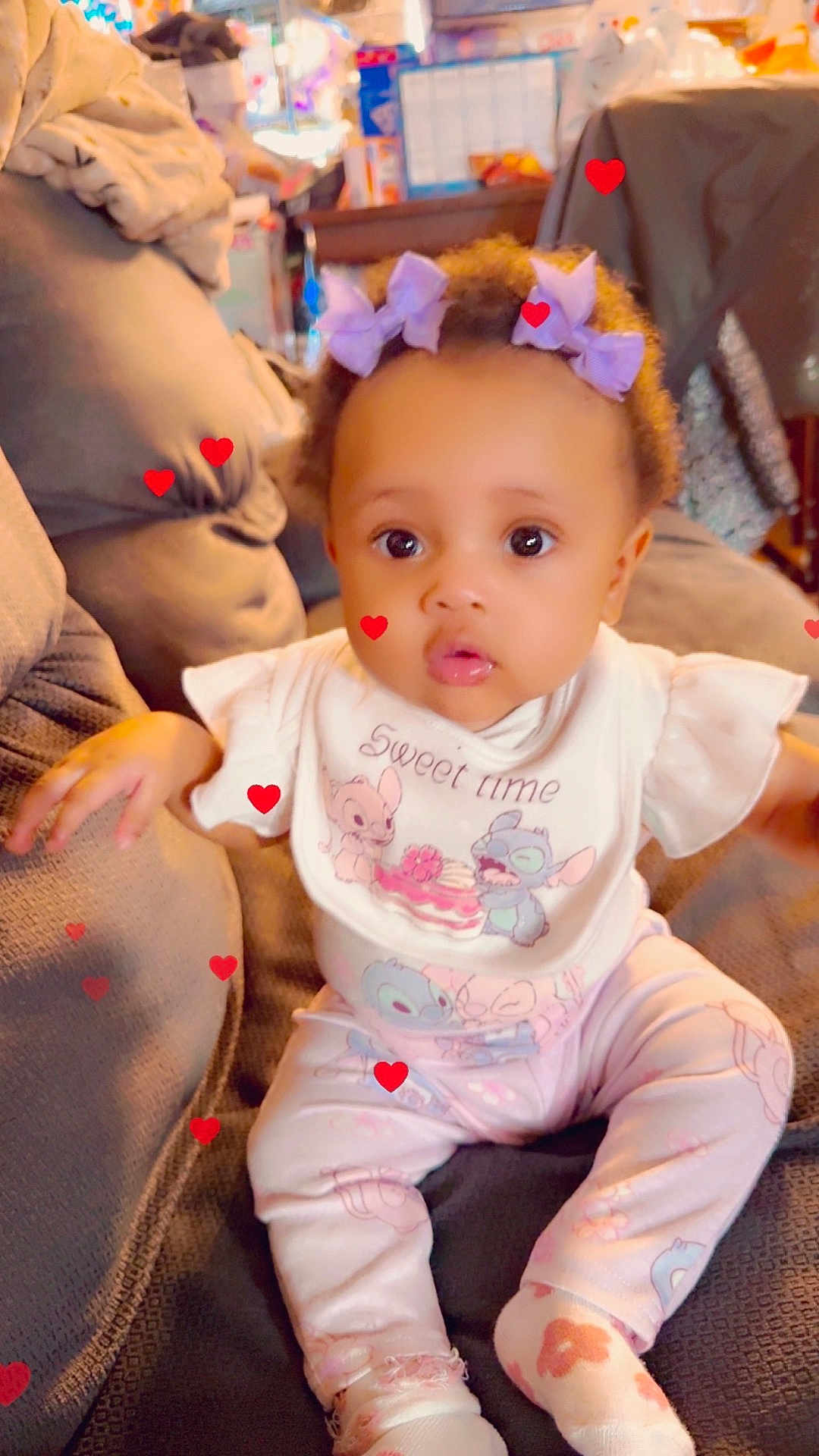 Tihira joined the competition — help win amazing prizes! baby, child, pajamas, bib, purple_bows, couch, indoor, heart_graphics, cute, infant, sitting, clothing, person, adorable, young_child, pink, soft_lighting, expression, portrait, home