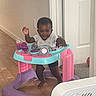 Isis is registered to the contest to win money with this photo: baby, blue, child, clothing, door, fan, floor, happy, indoor, person, pink, plastic, purple, smiling, standing, toy, walker, waving, wooden_floor, young_child