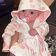 Elaina is registered to the contest to win money with this photo: baby, infant, pacifier, hooded_robe, pink, white, animal_print, person, arms, indoor, carpet, furniture, table, photo_frame, blanket, cute, child, young, portrait, clothing