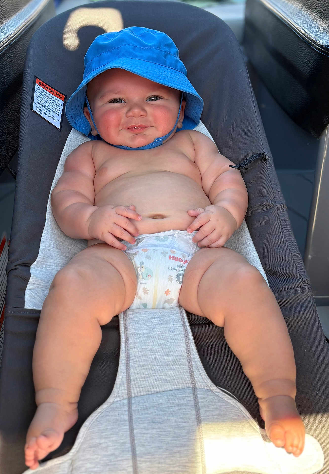 Stetson is registered to the contest to win money with this photo: baby, blue_hat, diaper, baby_seat, smiling, chubby, sunlight, skin, cute, child, infant, happy, outdoor, face, legs, feet, hands, rosy_cheeks, relaxing, sunhat