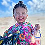 child, toddler, smiling, outdoor, sunny, blue_sky, clouds, floral_swimsuit, colorful_clothing, plastic_bag, red_slushy, happy, portrait, summer, vacation, cute, standing, sunshine, playful, young_child