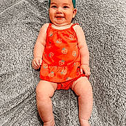 Jemma joined the competition — help win amazing prizes! baby, smiling, headband, orange_clothing, strawberry_pattern, blanket, lying_down, happy, infant, cute, child, soft_texture, cozy, portrait, skin, legs, arms, feet, indoors, bright_colors