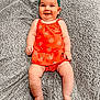baby, smiling, headband, orange_clothing, strawberry_pattern, blanket, lying_down, happy, infant, cute, child, soft_texture, cozy, portrait, skin, legs, arms, feet, indoors, bright_colors