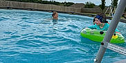 Jemma is registered to the contest to win money with this photo: child, pool, water, swimming, inflatable, float, backyard, fence, sky, clouds, smile, summer, outdoor, play, fun, trees, grass, swing_set, headband, person