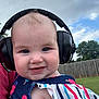 Jemma joined the competition — help win amazing prizes! baby, headphones, smile, outdoor, child, fence, grass, sky, clouds, colorful_clothing, summer, cute, portrait, head, blue_eyes, skin, person, playful, happy, infant