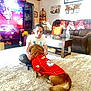 autumn_decor, basket, carpet, casual_clothing, couch, dog, flowers, football_jersey, holiday, home, indoor, interaction, living_room, person, pet, pumpkin_decor, smiling, sports, table, television
