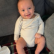 Lucas is registered to the contest to win money with this photo: baby, smiling, infant, sitting, blanket, plaid, couch, gray, happy, cute, child, indoors, face, skin, foot, hand, onesie, cozy, comfort, young