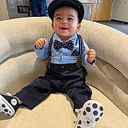 Kyson is registered to the contest to win money with this photo: baby, child, smiling, sitting, chair, indoors, clothing, bow_tie, hat, suspenders, footwear, person, furniture, happy, cute, portrait, casual, background, polka_dot, infant