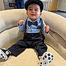 baby, child, smiling, sitting, chair, indoors, clothing, bow_tie, hat, suspenders, footwear, person, furniture, happy, cute, portrait, casual, background, polka_dot, infant