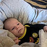 baby, infant, blanket, cushion, clothing, face, head, person, indoor, floor, rug, pattern, black_clothing, yellow_trim, patch, hand, wood_floor, baby_seat, comfort, resting