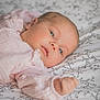 baby, infant, face, person, bed, blanket, fabric, pattern, pink_clothing, skin, head, hand, sleepwear, newborn, portrait, lying_down, soft_light, indoor, closeup, peaceful