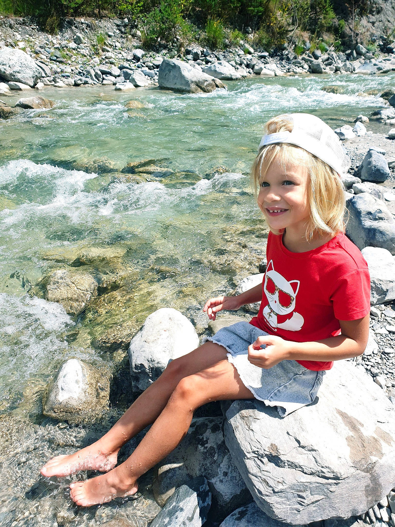 Victorine a rejoint le concours — aidez-le/la à gagner de superbes lots ! bank, bedrock, creek, foot, fun, grass, happy, human_leg, joy, landscape, leisure, people_in_nature, person, recreation, rock, sitting, smile, stream, thigh, toddler