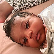 Egyptian is registered to the contest to win money with this photo: baby, infant, face, blanket, stars, bed, sleepwear, skin, person, newborn, lying_down, curly_hair, closeup, indoors, resting, soft_fabric, comfort, peaceful, adult_foot, casual