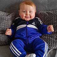 Timéo participe au concours pour gagner de l'argent avec cette photo : adidas, baby, blue_tracksuit, casual_clothing, child, couch, cozy, cute, grey, happy, home, indoor, person, plush_cushions, portrait, seated, smiling, socks, soft_texture, young_child