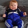 adidas, baby, blue_tracksuit, casual_clothing, child, couch, cozy, cute, grey, happy, home, indoor, person, plush_cushions, portrait, seated, smiling, socks, soft_texture, young_child