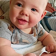 Danny is registered to the contest to win money with this photo: baby, child, smiling, blue_eyes, blanket, indoors, portrait, cute, infant, clothing, face, hand, furniture, home, person, toddler, cozy, happy, lying_down, casual