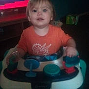 Atreus Reed joined the competition — help win amazing prizes! toddler, child, baby, sitting, activity_walker, toy, orange_shirt, indoors, living_room, television, portrait, face, eyes, looking_at_camera, curious, hands, colorful, dim_lighting, blurry, home