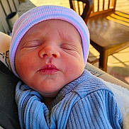 Zavier is registered to the contest to win money with this photo: newborn, baby, infant, sleeping, portrait, face, knit_hat, blue_clothing, onesie, outdoor, porch, wooden_chair, sunlight, cozy, peaceful, closed_eyes, swaddled, seated, photography, daylight