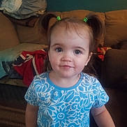 Valkyrie Rose is registered to the contest to win money with this photo: child, toddler, girl, portrait, face, smiling, pigtails, hair_bows, blue_shirt, floral_pattern, indoors, living_room, couch, blanket, home, seated, looking_at_camera, brown_hair, happy, photography