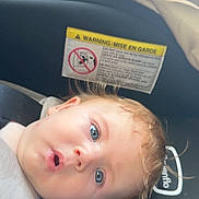 Hayes is registered to the contest to win money with this photo: baby, child, infant, car_seat, vehicle, portrait, face, blue_eyes, blond_hair, wide_eyed, surprised, lying_down, indoor, travel, safety_label, photograph, smartphone_screenshot, family, head, expression